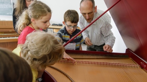 Eine Mann zeigt einer Gruppe Kindern ein offenes Cembalo
